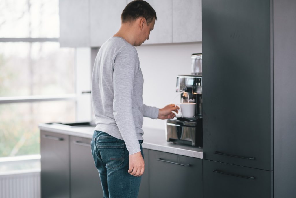 a man getting coffee from a coffee machine in the kitchen 